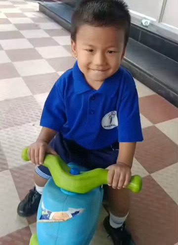 A smiling child riding a toy scooter at school